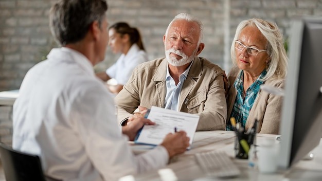 Senior couple consulting with healthcare worker about their insurance policy while having a meeting at clinic